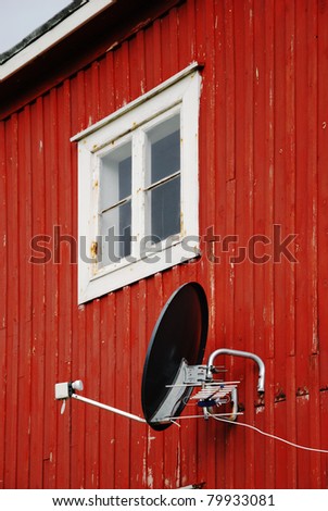 Satellite antenna on wall of small wooden house.