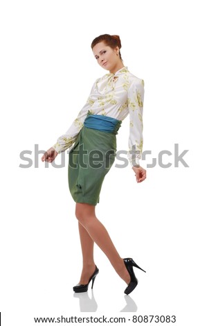 Young office worker is standing. The friendly woman is looking at the camera. She is wearing a stylish blouse, a green skirt and black pumps.