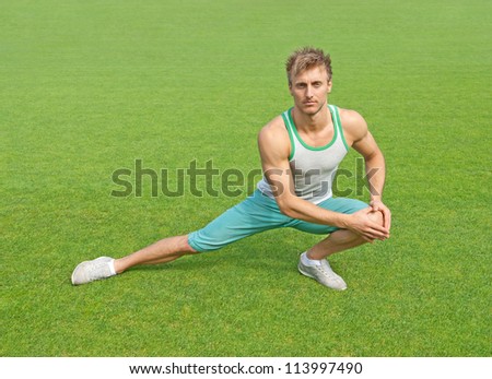 Fit young man exercising outdoors on green field.