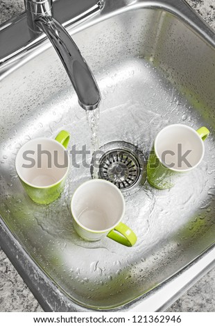 Washing green cups in the kitchen sink. Water running from the tap.