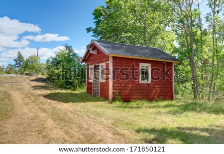 Traditional Swedish cabin painted in red color. Countryside in summer.