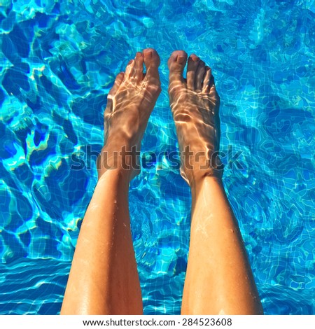 Female feet in blue water. Swimming pool with sun reflections.