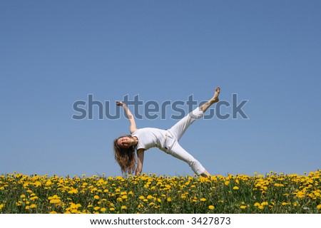 Smiling young woman in summer white clothes exercising in flowering dandelion field.
