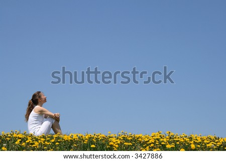 Girl in white clothes sitting in a flowering dandelion field.