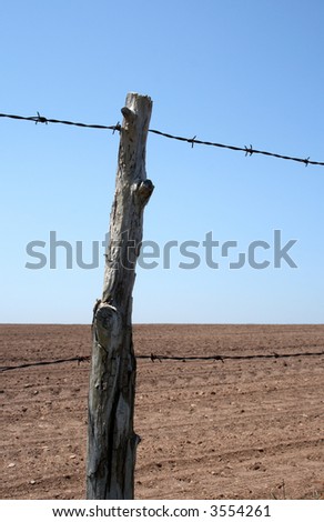 Old barbed wire farm fence and cultivated farmland in spring.