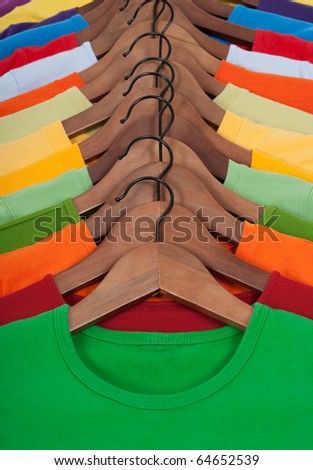 Choice of vibrant colorful t-shirts on wooden hangers.