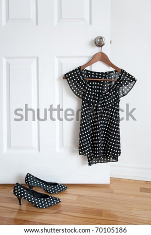 Black and white polka dot shoes and stylish blouse on a hanger.