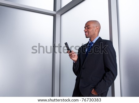 Young businessman beside an office window looking at his cell phone, smiling.