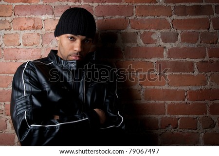 Tough street guy with his arms crossed, leaning against the brick wall.