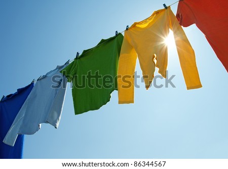 Colorful clothes hanging to dry on a laundry line and sun shining in the blue sky.