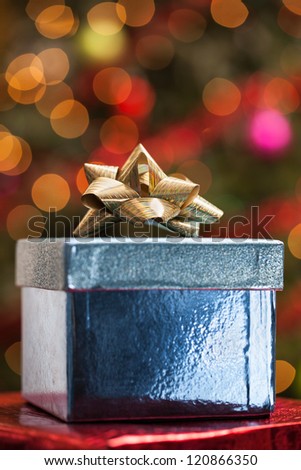 Christmas present with bow under a tree with defocused lights and ornaments