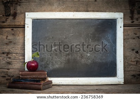 Vintage chalkboard with stack of books and apple on rustic wooden table and vintage filtered effect