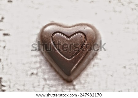 Closeup of a chocolate heart on a vintage white painted table with crackled paint with antique matte filtered effect