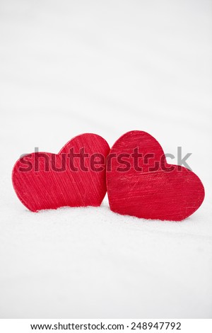 Two red painted wooden hearts covered in real fresh snow in winter for Valentines Day