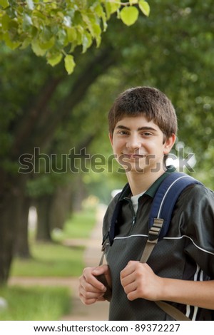 Portrait of a tween boy student wearing backpack outdoors under trees