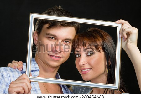 Young couple having fun making faces through tablet frame