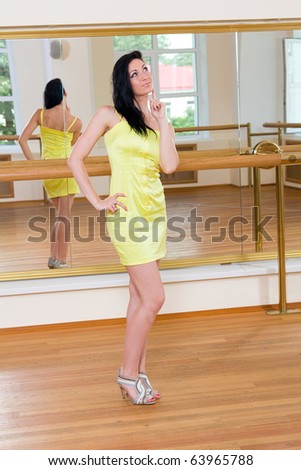 thoughtful beautiful woman in a little yellow dress stands in front of a large mirror