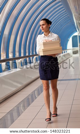 young woman in a white blouse is in blue corridor business center and carries boxes