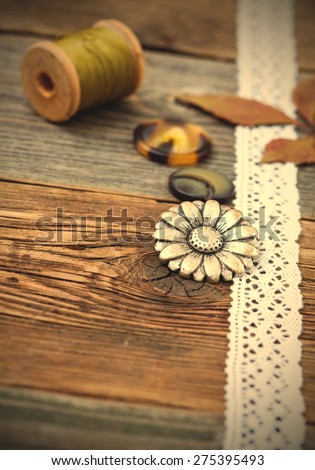 vintage buttons with lace tape and spools of thread on aged wooden surface. Still life. Focus located on button flower. instagram image retro style