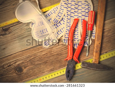 vintage hammer, old pliers, screwdriver, tape measure, gloves and safety glasses on aged  textured boards bench. still life with working tools. instagram image filter retro style