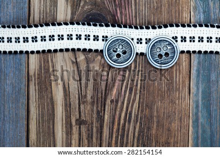 Vintage ribbon with embroidered pattern and ancient classical buttons on the old textured boards