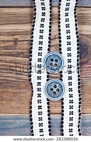 Vintage tape with embroidered pattern and ancient classical buttons on the old textured boards