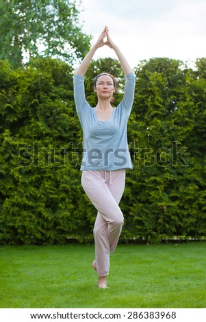 pretty adult woman doing yoga on green grass in park