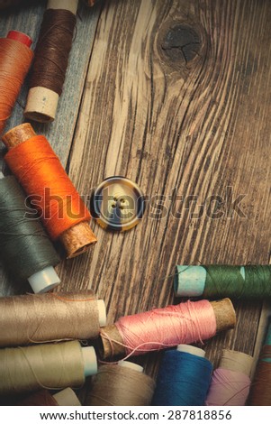 Vintage spools with varicolored threads and old button on old tailoring table. instagram image filter retro style