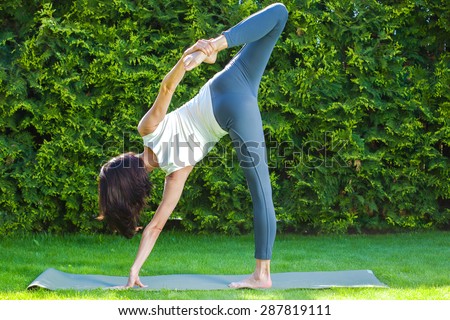 pretty adult woman doing yoga on green grass in park at summer day