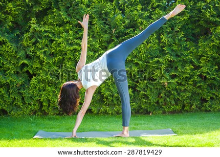 beautiful adult woman doing yoga on green grass in park