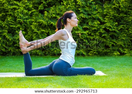 pretty adult woman doing yoga on green grass at summer day in park