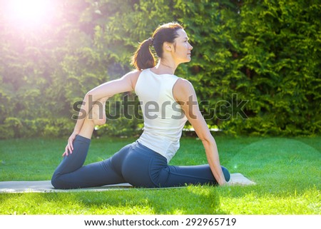 beautiful adult woman doing yoga on green grass at summer day in park at summer morning. lens flare effect is applied deliberately