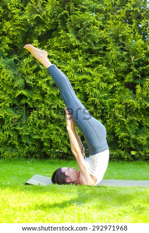 woman doing yoga on green grass in park at summer day