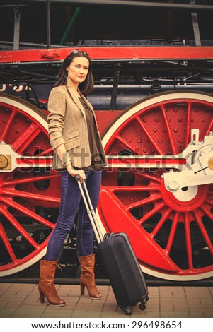 retro journey for a beautiful lady. pretty adult woman with luggage near the huge wheels of an old steam locomotive to travel. instagram image filter retro style