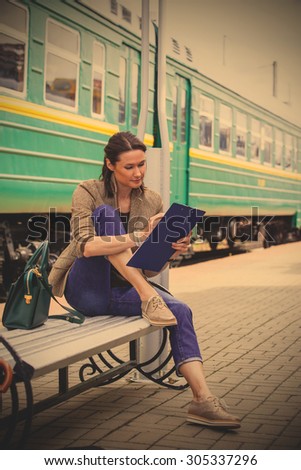 beautiful adult woman takes notes in notepad.He is sits on a bench and waits for the train retro travel by railroad. instagram image filter retro style