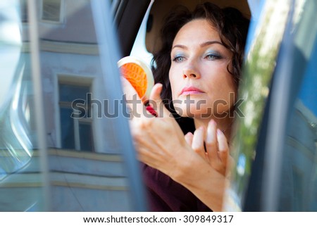 pretty middle-aged woman looking in the mirror carefully checked the makeup on face, in the car salon