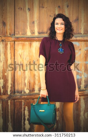 beautiful middle-aged woman in a burgundy dress and green handbag near aged doors. instagram image filter retro style