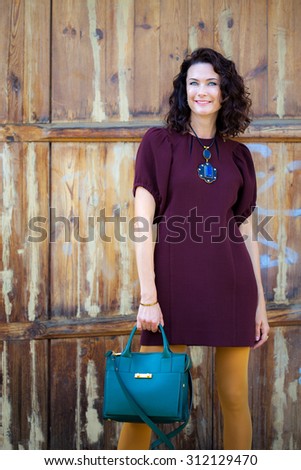beautiful middle-aged woman in a burgundy dress and green handbag near aged doors