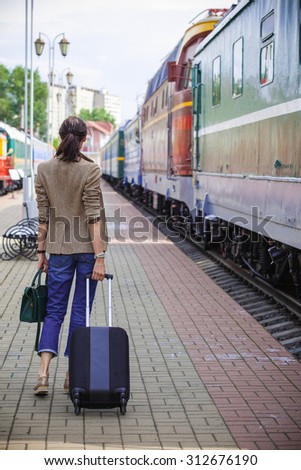 woman with luggage walking on the platform along the passenger train. returning from vacation