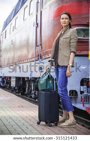 beautiful middle-aged woman with luggage goes on the retro train in the railway trip