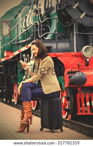 beautiful middle-aged woman sitting on a trunk road and uses the phone near the old steam locomotive. instagram image filter retro style