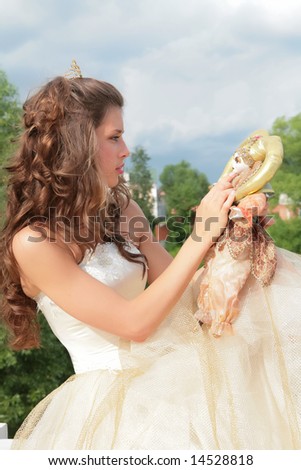 princess in white-golden gown plays with loved doll on background cloudy sky