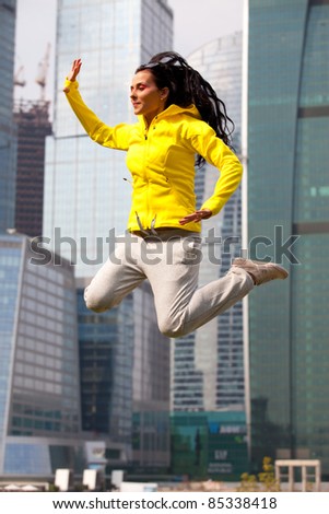 brunette in a yellow blazer jumping on the background the skyscrapers of a big city