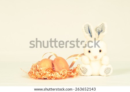 Toy fluffy easter bunny with orange eggs in nest sits on white background and looking at camera. There is copy space.