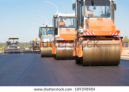 Pneumatic steam road rollers machines compacting fresh asphalt during highway construction works on tracked paver equipment background