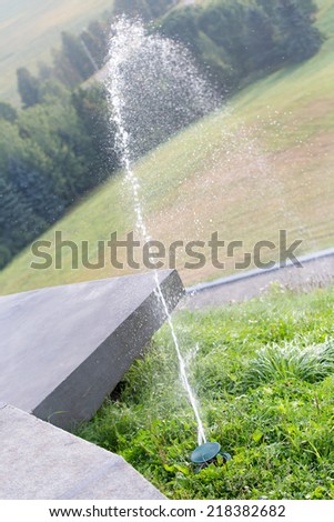 Water jet of a sprinkler head watering green grass lawn