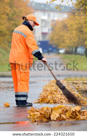 Female street sweeper caretaker cleaning city pavement from dead leaves