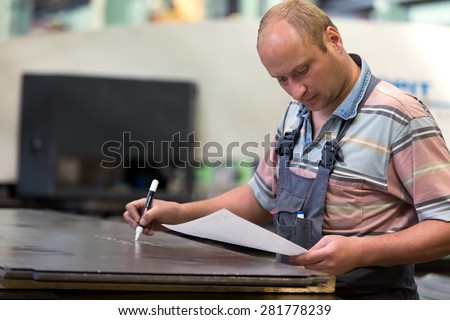 Factory man worker marking metal sheet in workshop during technological process of manufacturing workpiece