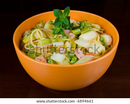Healthy pasta dish with peas, leeks and bacon, in orange bowl on dark wooden table