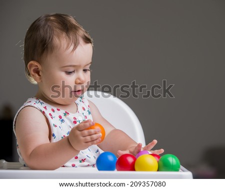 cute baby girl seating in a chair and playing with color full balls